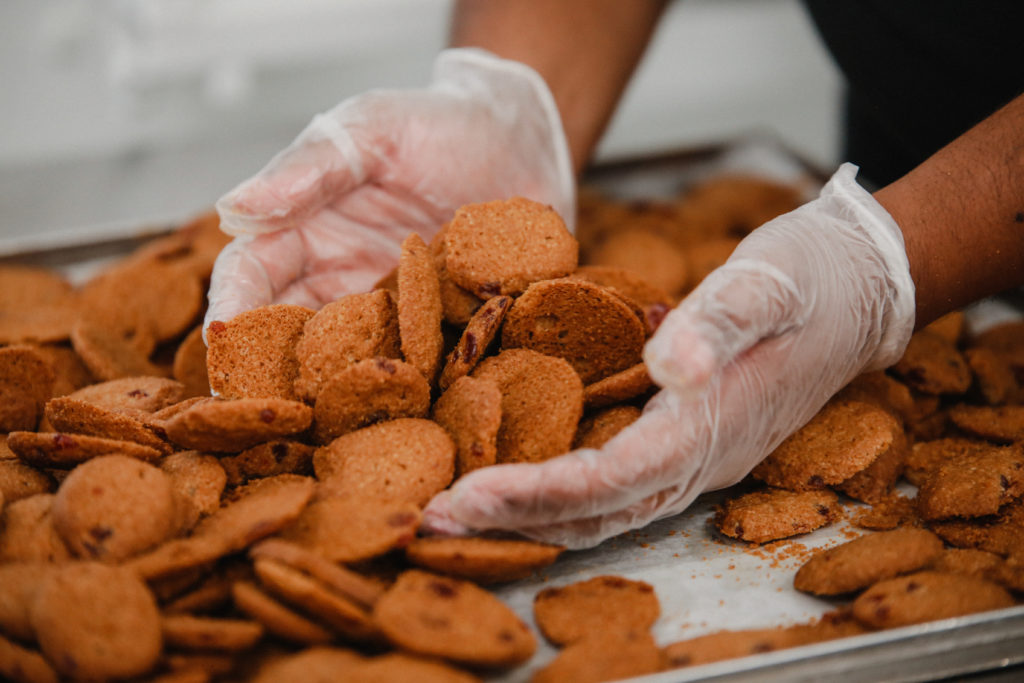 Sobre una bandeja, múltiples galletas de chocolate chip en las manos de una empleada